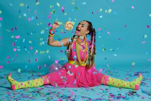 Lovely girl with a multi-colored braids hairstyle and bright make-up, posing in studio with lollipop, air balloons and confetti against a blue background. photo