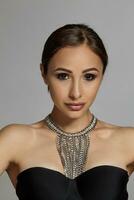 Close up portrait of a brunette model girl with professional evening make-up, wearing a black bra and necklace, posing on gray background. photo