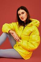 Studio portrait of young brunette woman sitting on the floor in yellow down jacket and grey blue panty hoses or stockings photo