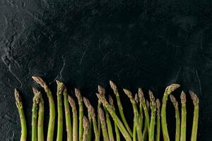 Raw uncooked green asparagus spears on black slate background. Concept of healthy nutrition, food and seasonal vegetables harvest. Close up photo