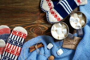Two cups of hot cocoa or chocolate with marshmallow, mittens, christmas decor and fir tree on wooden rustic background from above. photo