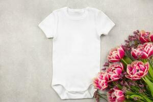 White baby girl or boy bodysuit mockup flat lay with tulip flowers on gray concrete background. Design onesie template, print presentation mock up. Top view. photo