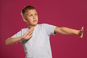 Close-up portrait of a blonde teenage boy in a white t-shirt posing against a pink studio background. Concept of sincere emotions. photo