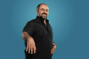 Close-up portrait of a brunet middle-aged man with beard, dressed in a black t-shirt and posing against a blue background. photo