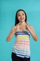 Brunette woman with long hair, dressed in striped shirt and black leggings, posing against blue studio background. Sincere emotions. Close-up. photo