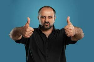 Close-up portrait of a brunet middle-aged man with beard, dressed in a black t-shirt and posing against a blue background. photo