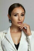 Close up portrait of a brunette model girl with professional evening make-up, wearing a white jacket with black bra, posing on gray background. photo