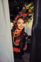 Brunette girl in a white ukrainian authentic national costume and a wreath of flowers is posing against a terrace. Close-up. photo