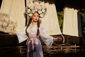 Brunette girl in a white ukrainian authentic national costume and a wreath of flowers is posing against a terrace. photo