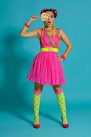 Lovely girl with a multi-colored braids hairstyle and bright make-up, posing in studio against a blue background, holding a lollipop in her hand. photo