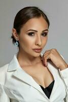 Close up portrait of a brunette model girl with professional evening make-up, wearing a white jacket with black bra, posing on gray background. photo