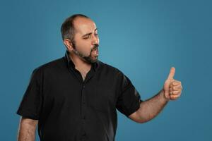 Close-up portrait of a brunet middle-aged man with beard, dressed in a black t-shirt and posing against a blue background. photo