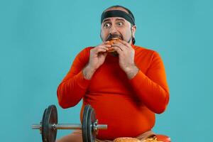 Middle-aged man with beard, dressed in a red turtleneck, headband, posing with burgers and french fries. Blue background. Close-up. Fast food. photo