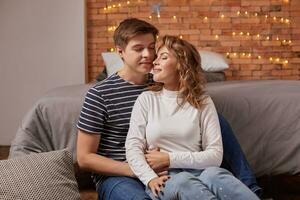 Portrait of a young loving couple resting on a grey couch together at home and hugging photo