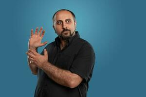 Close-up portrait of a brunet middle-aged man with beard, dressed in a black t-shirt and posing against a blue background. photo