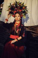 Brunette girl in a white ukrainian authentic national costume and a wreath of flowers is posing against a terrace. Close-up. photo