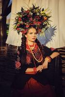 morena niña en un negro y rojo bordado ucranio auténtico nacional disfraz y un guirnalda de flores es posando en contra un terraza. de cerca. foto