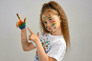 Little girl in white t-shirt is posing standing isolated on white and gesticulating with her painted in different colors palms. Art studio. Close-up. photo