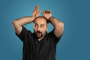 Close-up portrait of a brunet middle-aged man with beard, dressed in a black t-shirt and posing against a blue background. photo