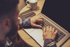 Young man drinking coffee in cafe and using laptop. Man's hands photo