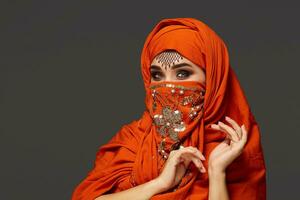 Studio shot of a young charming woman wearing the terracotta hijab decorated with sequins and jewelry. Arabic style. photo