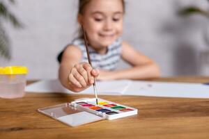 inspirado pequeño niña a el mesa dibujar con pinturas foto