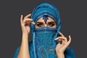 Studio shot of a young beautiful woman wearing the blue hijab decorated with sequins and jewelry. Arabic style. photo