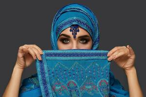 Studio shot of a young beautiful woman wearing the blue hijab decorated with sequins and jewelry. Arabic style. photo