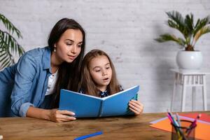 Mom helps my daughter do her homework in the kitchen. Mom and daughter are engaged in reading. photo