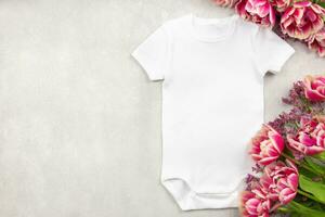 White baby girl or boy bodysuit mockup flat lay with tulip flowers on gray concrete background. Design onesie template, print presentation mock up. Top view. photo