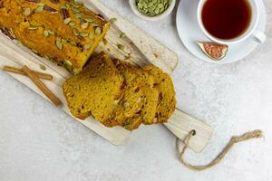 Pumpkin bread, cake on a wooden cutting board with pecan nuts, pumpkin seeds and cinnamon spices on a light gray background. Top view. photo