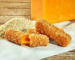 Deep-fried cheddar cheese sticks in breadcrumbs on wooden table photo