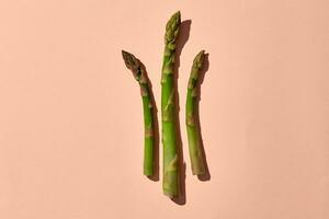 Three green asparagus spears on pink background. Concept of healthy food and seasonal vegetables harvest. Close up, copy space photo