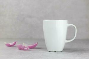Classic white mug mockup with flowers petals on light gray concrete background. Valentines, mothers, womens, 8 march or birthday concept. Side view. Copy space. photo