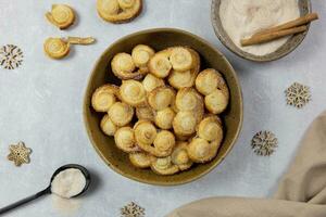 Puff pastry eyelet, Palmier cookies in a bowl with cinnamon and sugar on the light concrete background. Top view. photo