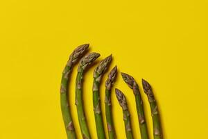 Ripe uncooked green asparagus spears against yellow background. Healthy nutrition, food and seasonal vegetables. Close up, flat lay, top view photo