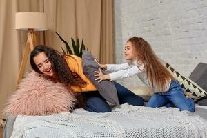 Young mom and daughter fooling around with pillow fights on the bed photo