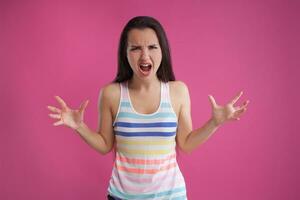 Brunette woman with long hair, dressed in colorful striped shirt, posing against pink studio background. Sincere emotions. Close-up. photo