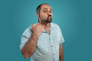 Close-up portrait of a brunet middle-aged man with beard, dressed in a light checkered shirt and posing against a blue background. photo