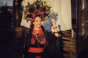 morena niña en un negro y rojo bordado ucranio auténtico nacional disfraz y un guirnalda de flores es posando en contra un terraza. de cerca. foto