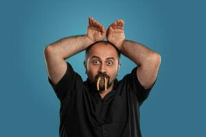 Close-up portrait of a brunet middle-aged man with beard, dressed in a black t-shirt and posing against a blue background. photo