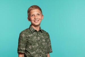 Close-up portrait of a blonde teenage boy in a green shirt with palm print posing against a blue studio background. Concept of sincere emotions. photo