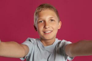de cerca retrato de un rubia Adolescente chico en un blanco camiseta posando en contra un rosado estudio antecedentes. concepto de sincero emociones foto
