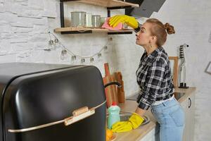 mujer en guantes limpieza mueble con trapo a hogar cocina. foto