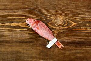 Salted sun-dried red mullet with label on tail on wooden table photo