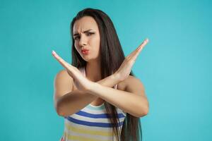 Brunette woman with long hair, dressed in colorful striped shirt, posing against blue studio background. Sincere emotions. Close-up. photo