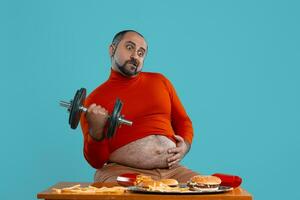 Close-up portrait of a middle-aged man with beard, dressed in a red turtleneck, posing with burgers and french fries. Blue background. Fast food. photo