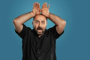 Close-up portrait of a brunet middle-aged man with beard, dressed in a black t-shirt and posing against a blue background. photo