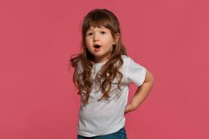 Close-up portrait of a little brunette girl dressed in a white t-shirt posing against a pink studio background. Sincere emotions concept. photo