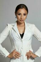 Close up portrait of a brunette model girl with professional evening make-up, wearing a white jacket with black bra, posing on gray background. photo